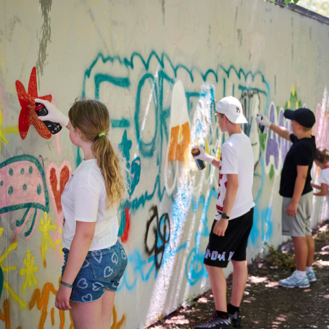 Jugendliche sprayen Grafittis an eine Wand.