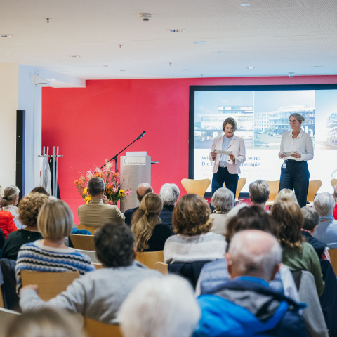 Saal mit Gästen und Moderatorinnen auf der Bühne