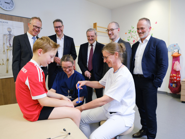 Die Ärztin untersucht einen Jungen, im Hintergrund steht die Gruppe.